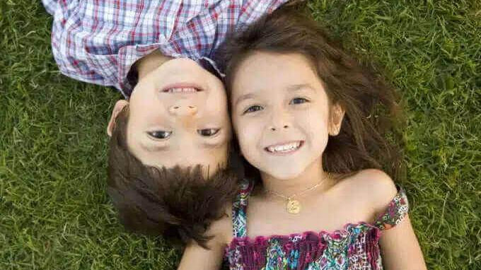 Crianças sorrindo deitadas na grama, representando a relação entre irmãos e a diferença de idade.