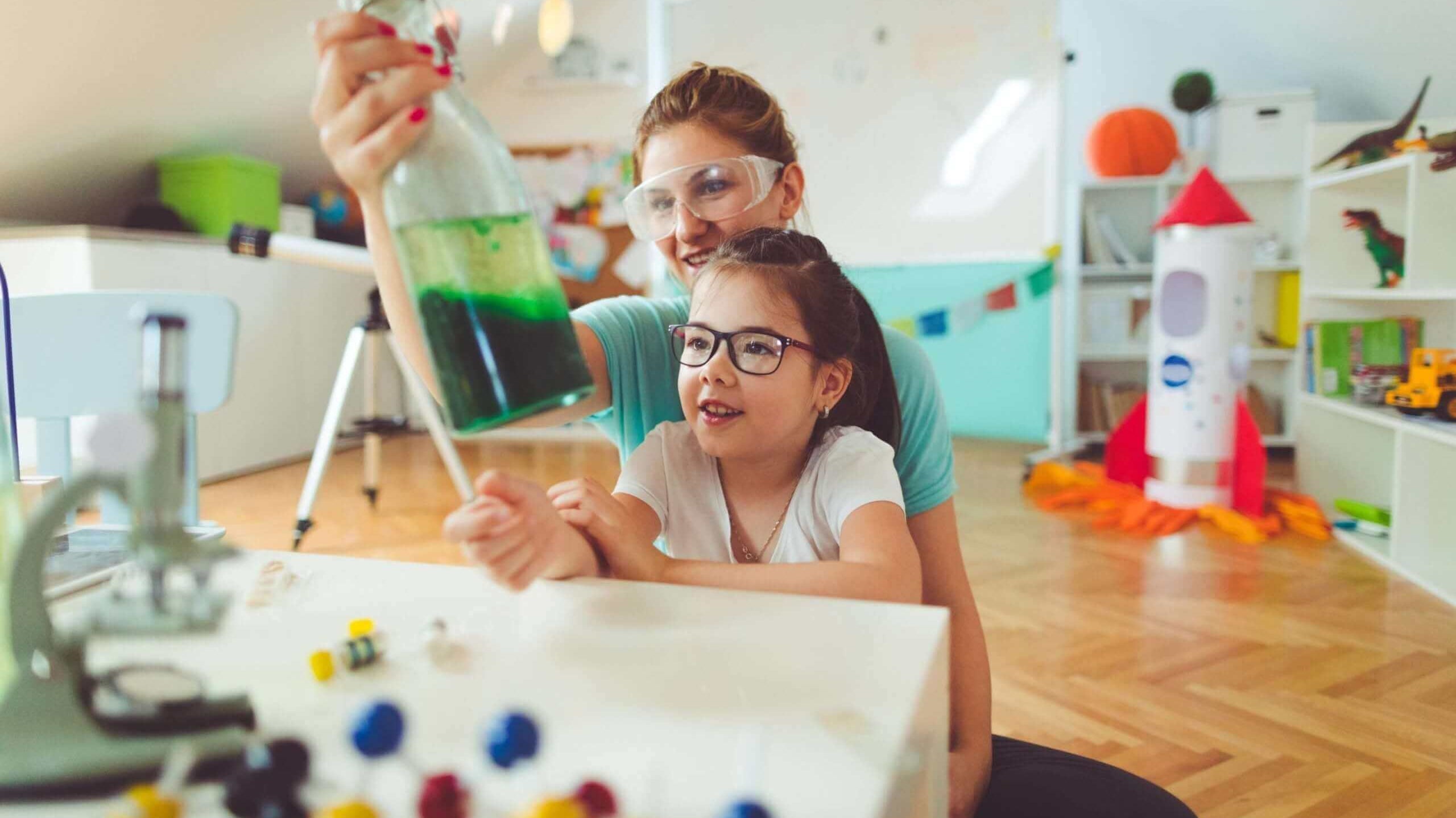 Mãe e filha realizando experimento científico com frascos coloridos em ambiente divertido e educativo.