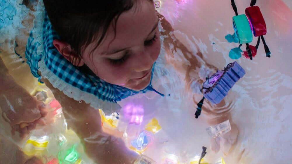 Criança se divertindo na banheira com Glo Pals iluminados em contato com a água, promovendo brincadeiras sensoriais.
