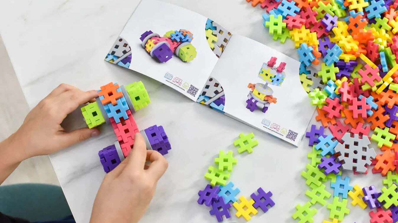 Child building a colorful Meli Blocks creation with a guidebook and scattered blocks on a table.