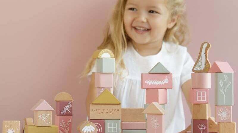 Garotinha sorrindo enquanto constrói com blocos de madeira coloridos e decorados. Jogos criativos para crianças pequenas.