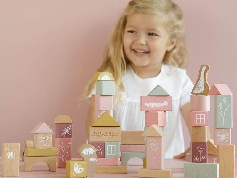 Garotinha sorrindo enquanto constrói com blocos de madeira coloridos e decorados. Jogos criativos para crianças pequenas.