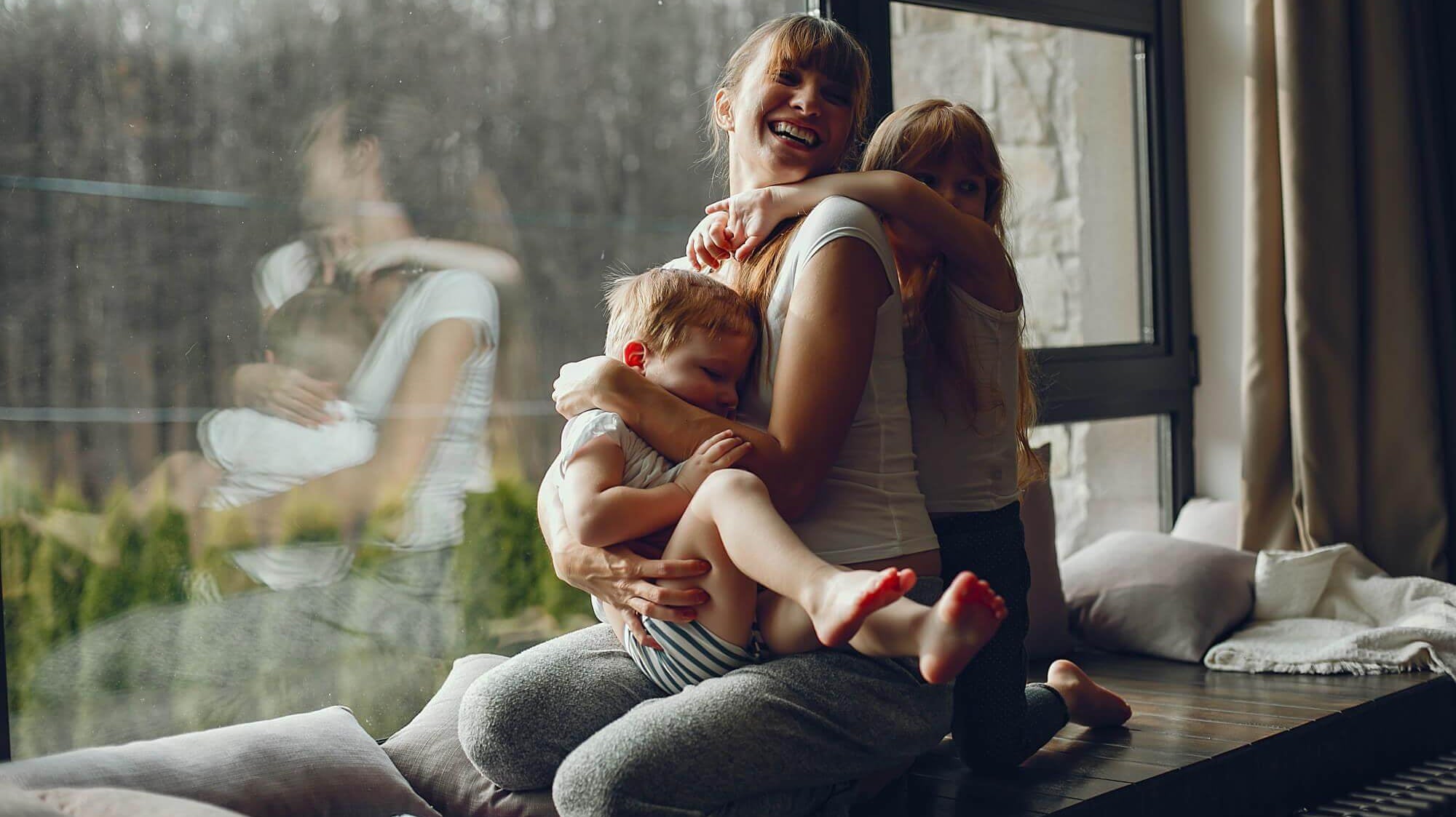 Mãe divertida brincando com suas duas crianças em um dia chuvoso, cercada por uma atmosfera acolhedora.