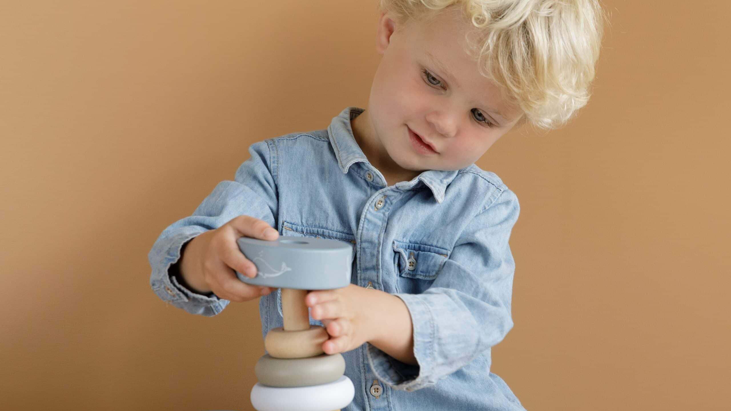 Criança brincando com brinquedos de madeira, empilhando peças coloridas sobre uma mesa.