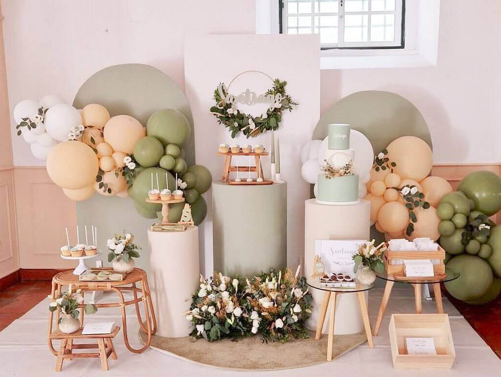 Decoração moderna de baby shower com balões, bolos e mesas elegantes em tons suaves de verde e bege.