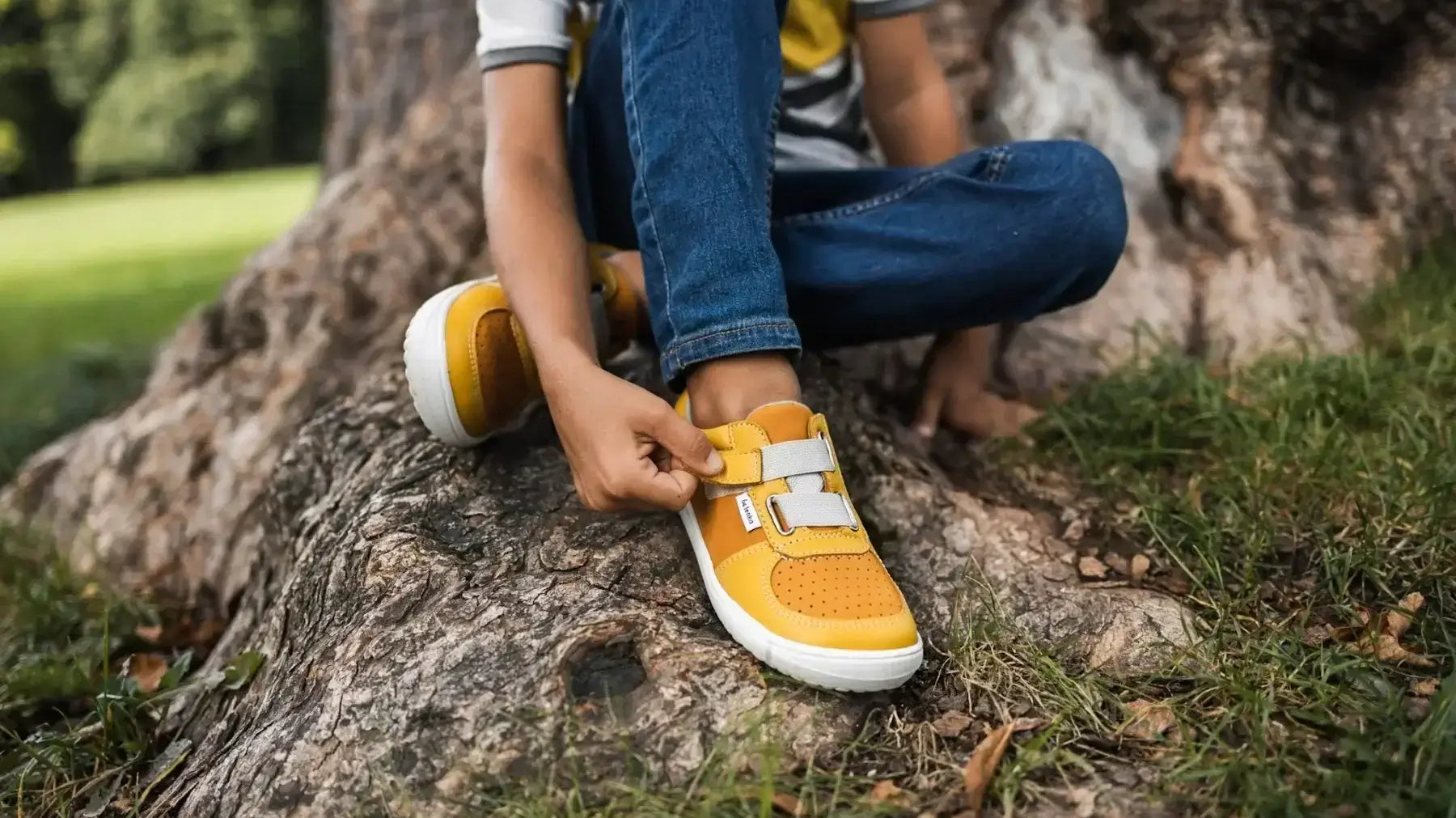Criança amarrando calçado infantil amarelo em ambiente natural, ideal para conforto e desenvolvimento saudável dos pés.