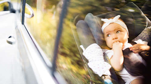 Bebé sentado em cadeira de segurança no carro, olhando pela janela durante a viagem.