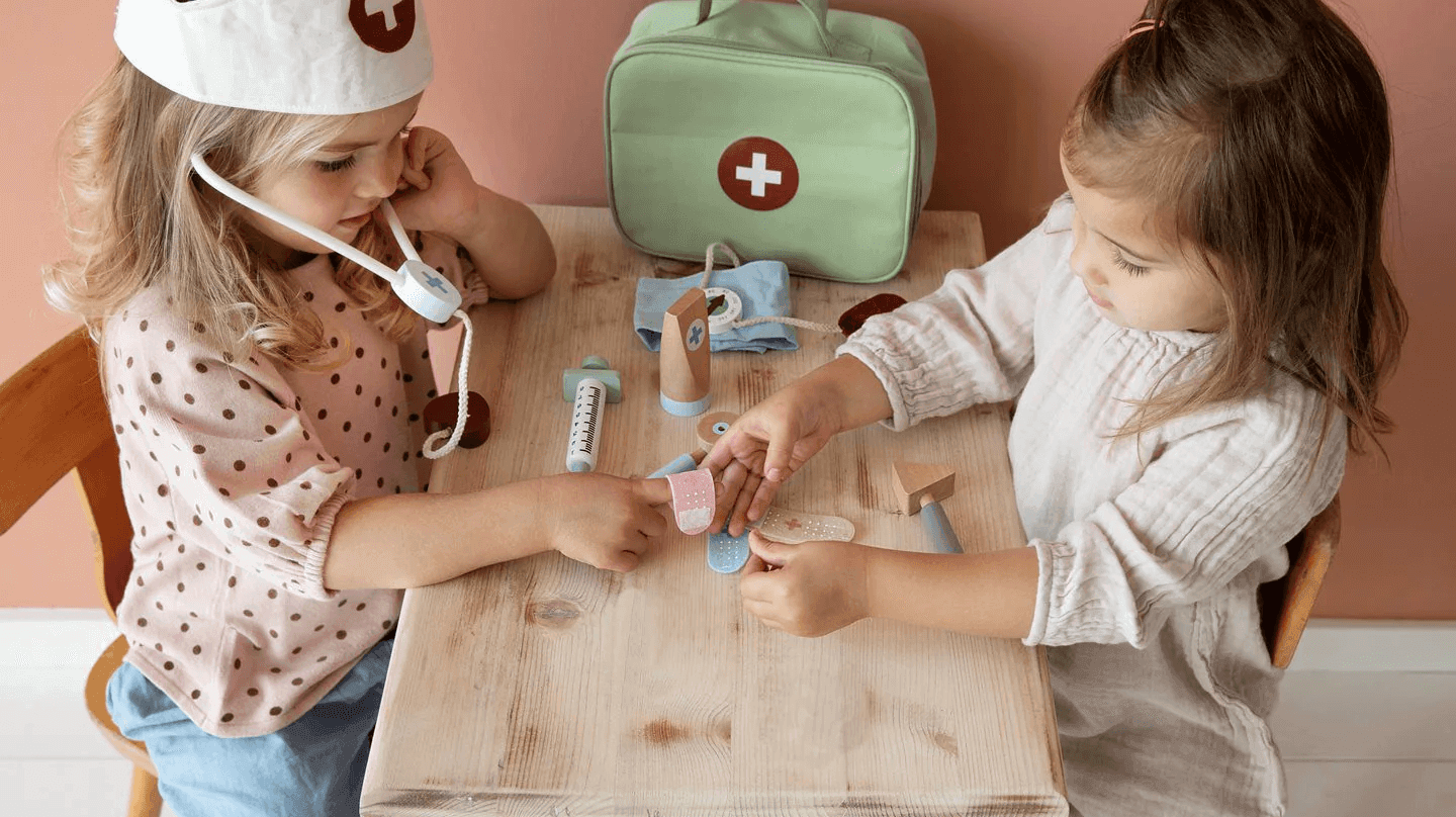 duas crianças brincando de médica com brinquedos de veterinário e uma maleta em mesa de madeira.