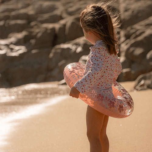 Child on the beach holding a Boia Little Dutch float with pink flowers, ready for summer fun.