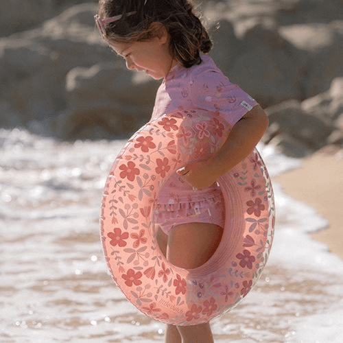 Little Dutch pink flower swimming ring held by a child on the beach, perfect for summer fun.