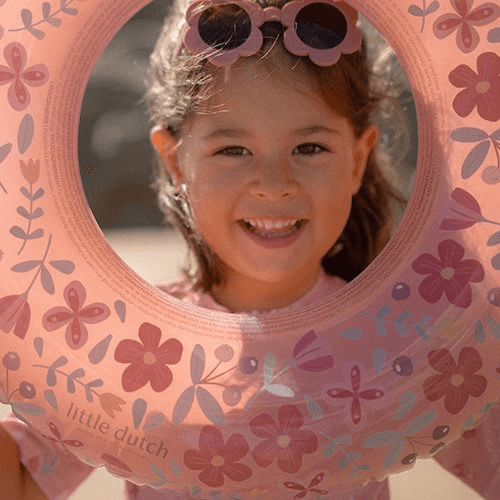 Smiling girl with sunglasses holding a pink flower-patterned swimming ring by Little Dutch.