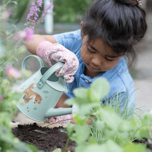 Criança regando plantas no jardim com regador da Little Dutch, parte do conjunto de jardinagem 10 peças.