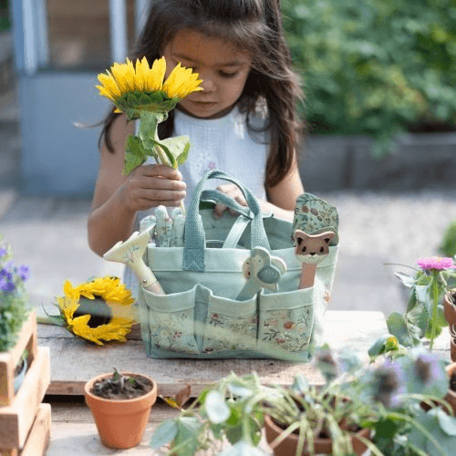 Criança segurando flor com conjunto de jardinagem Little Dutch em fundo natural e vasos de plantas.