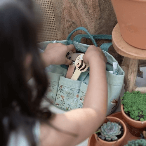 Criança retirando ferramentas de jardinagem de um conjunto da Little Dutch em um ambiente natural.