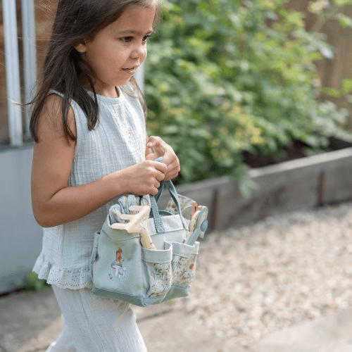 Garota pequena segurando um conjunto de jardinagem da Little Dutch enquanto explora o jardim.