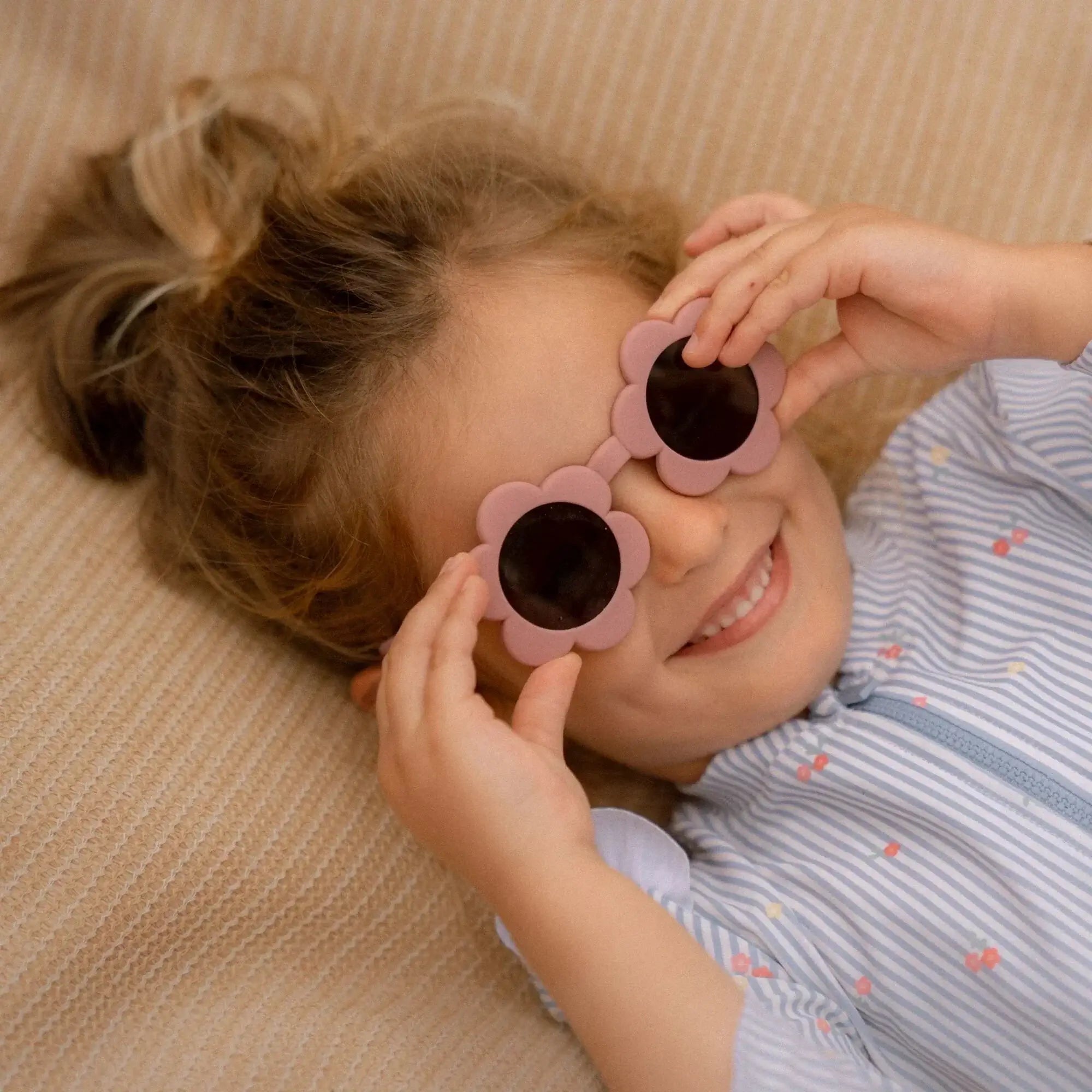 Criança usando óculos de sol Flower Pink da Little Dutch, sorrindo e se divertindo em um ambiente descontraído.
