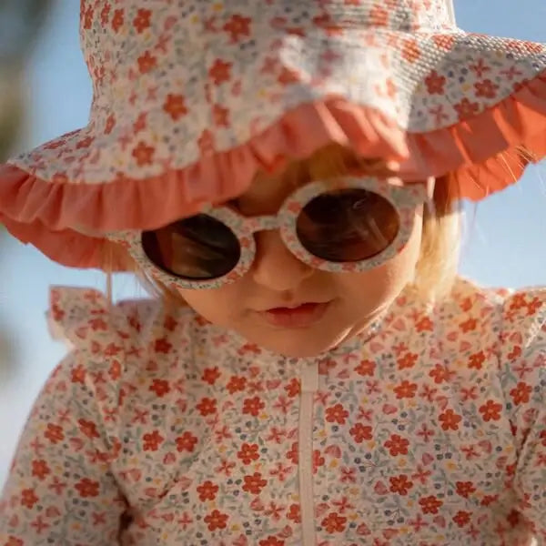 Criança usando óculos de sol redondos e chapéu florido, ideal para dias ensolarados.