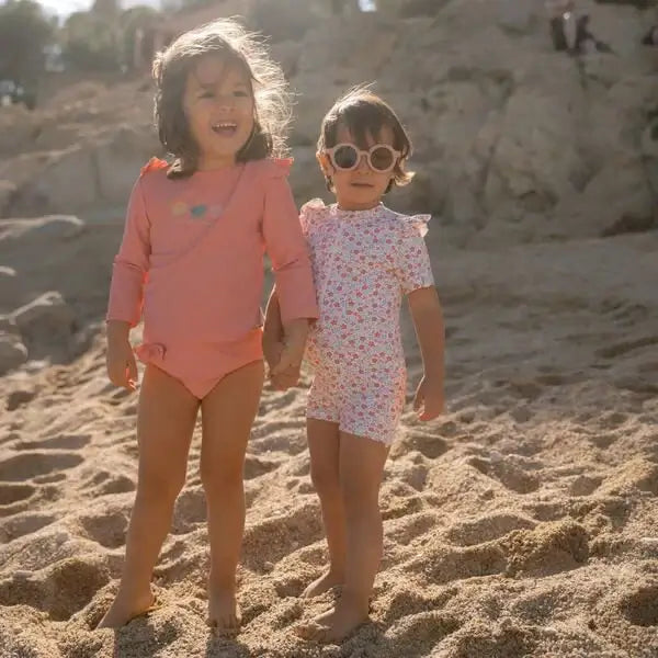 Duas meninas sorridentes na praia usando óculos de sol e roupas de banho, aproveitando um dia ensolarado.