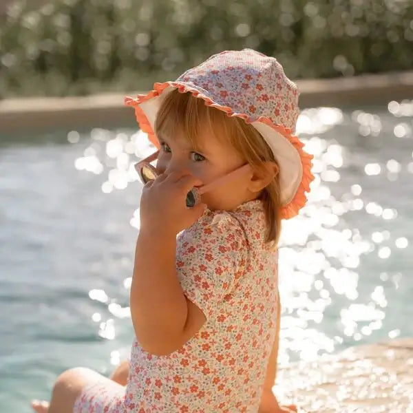 Menina com óculos de sol e chapéu, estilo verão, perto da piscina com reflexos de luz.
