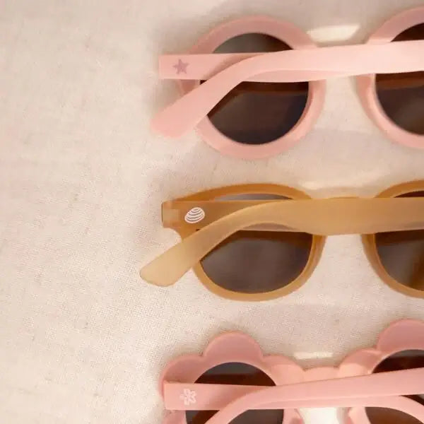 Óculos de sol infantis em diferentes estilos, incluindo redondos rosa e colores claros, sobre um fundo neutro.