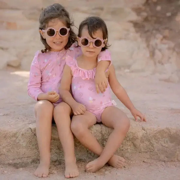 Duas meninas sorrindo usando óculos de sol Round Light Pink da Little Dutch, sentadas em um lugar ensolarado.