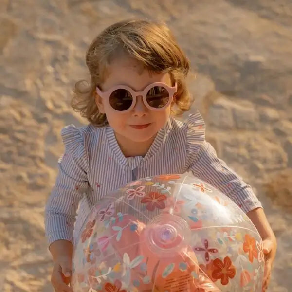 Criança usando óculos de sol redondos rosa claro da Little Dutch com bola colorida na praia.