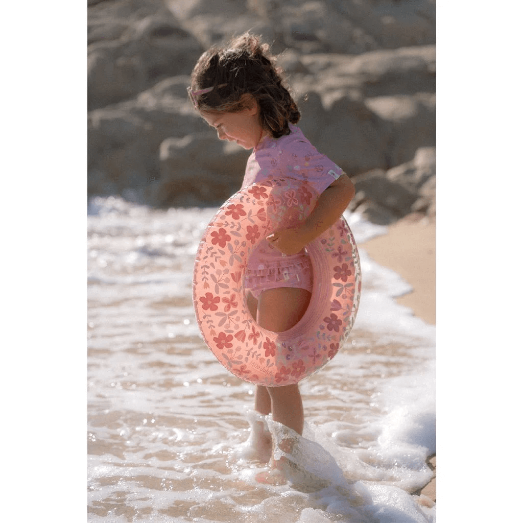 Child enjoying the beach with a pink flower swimming float by Boia Little Dutch, perfect for summer fun.