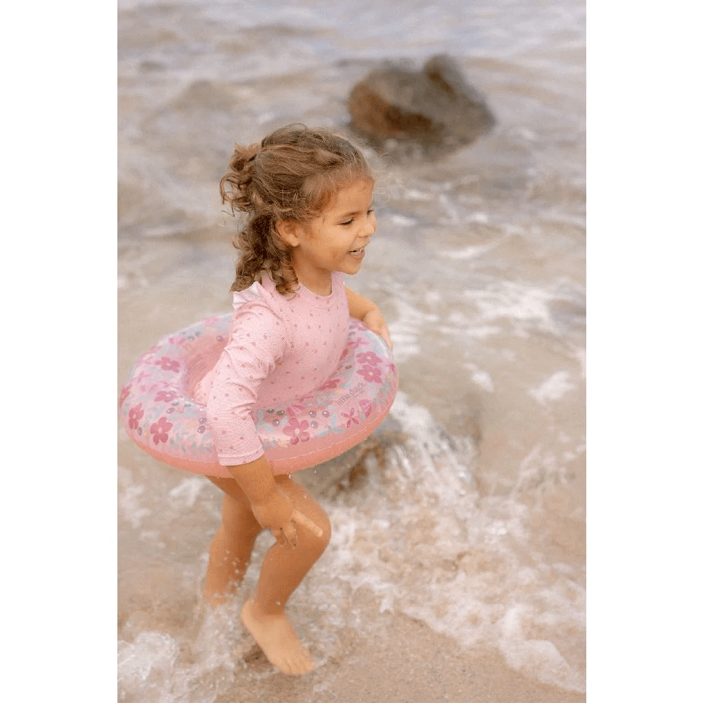 Child playing in the water with a pink flower swimming ring from Boia Little Dutch, enjoying a fun beach day.