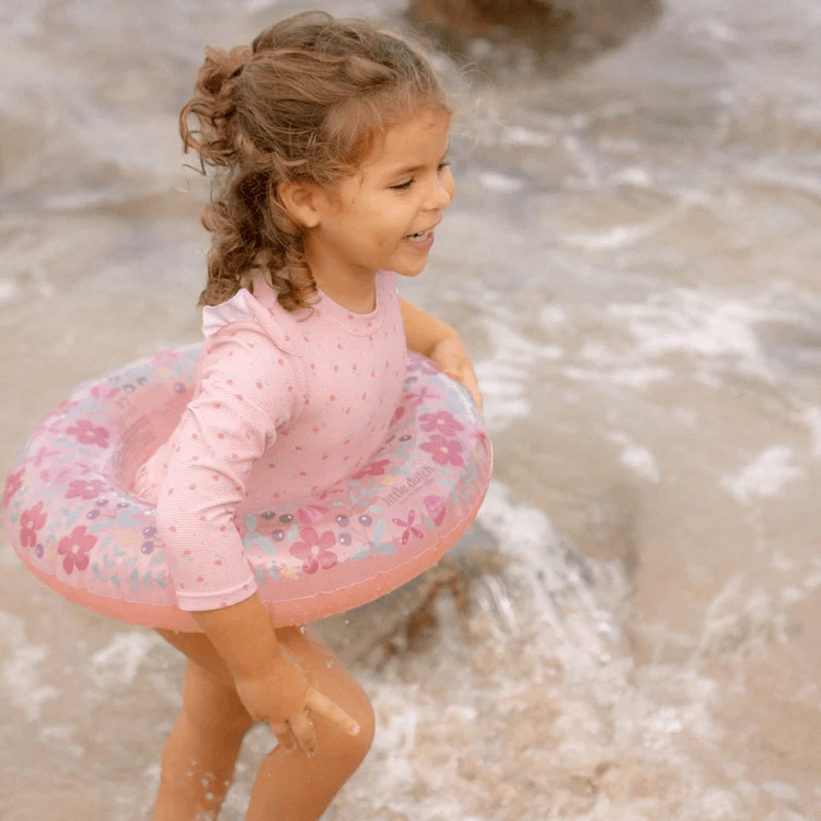 Child playing in the water with a Little Dutch pink flower swim ring, enjoying summer fun and splashing.