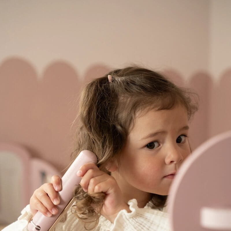 Criança usando o Conjunto de Cabeleireiro Little Dutch com uma prancha de alisar em um salão de beleza imaginário.