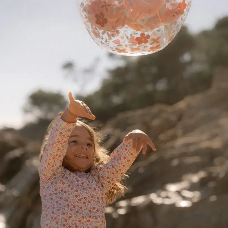 A joyful child playing with a 3D Pink Flowers beach ball by the seaside, surrounded by nature.