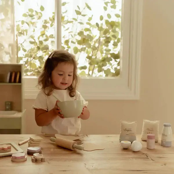 Menina brincando com o Conjunto de Pasteleiro Little Dutch, segurando uma taça de mistura em uma cozinha de brincar.