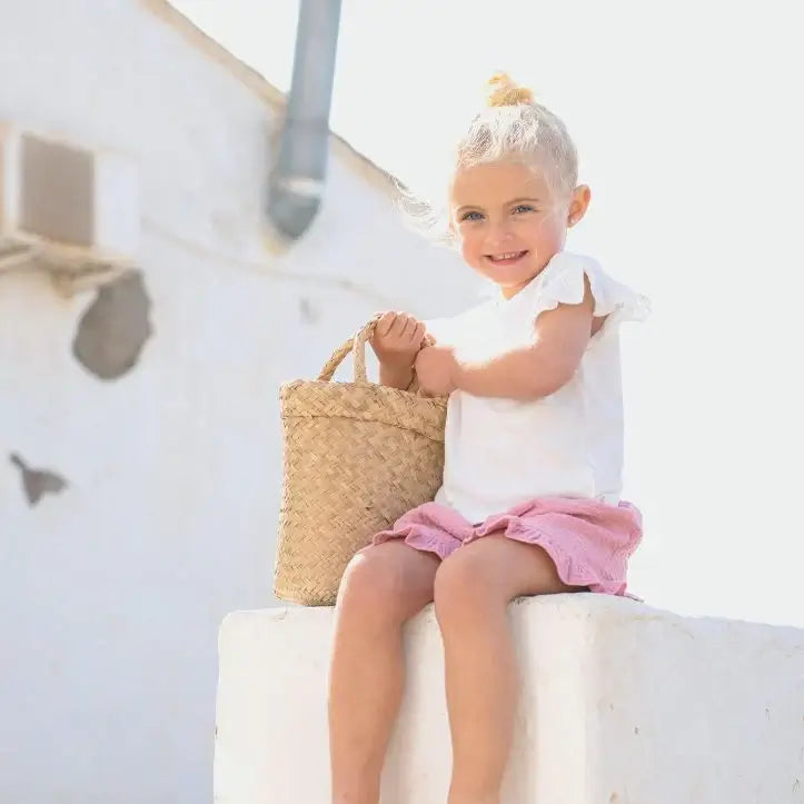 Criança sorridente usando sandálias Igor tamanho 23, segurando uma cesta de palha, em um ambiente de verão.