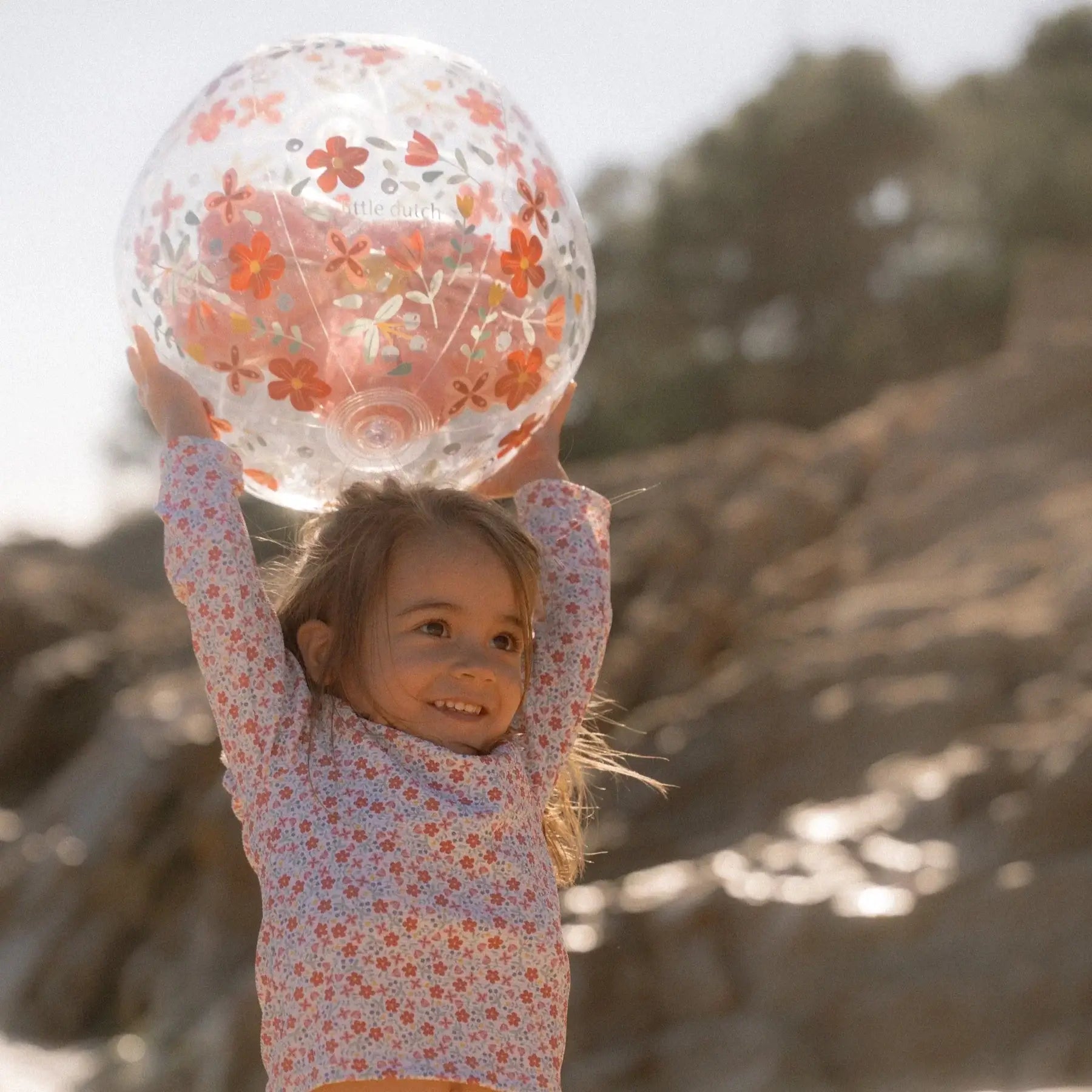 Criança alegre segurando a bola insuflável de praia 3D Pink Flowers da Little Dutch ao ar livre.