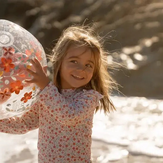 Girl playing with a 3D inflatable beach ball featuring pink flowers by the shore.