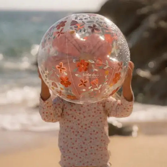 Criança segurando bola insuflável de praia 3D com flores pink à beira-mar, divertida e colorida.