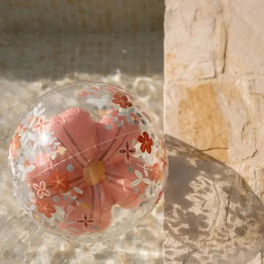 Bola insuflável de praia 3D com flores rosas, flutuando na água ao lado de uma piscina.