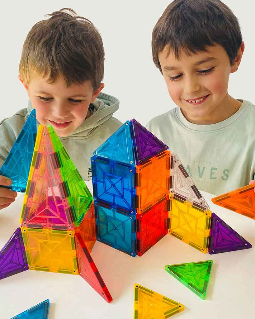 Two boys joyfully building a colorful structure with geometric magnetic tiles, showcasing creativity and play.