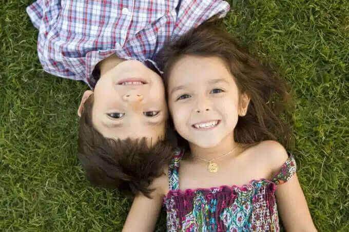 Crianças sorrindo deitadas na grama, representando a relação entre irmãos e a diferença de idade.