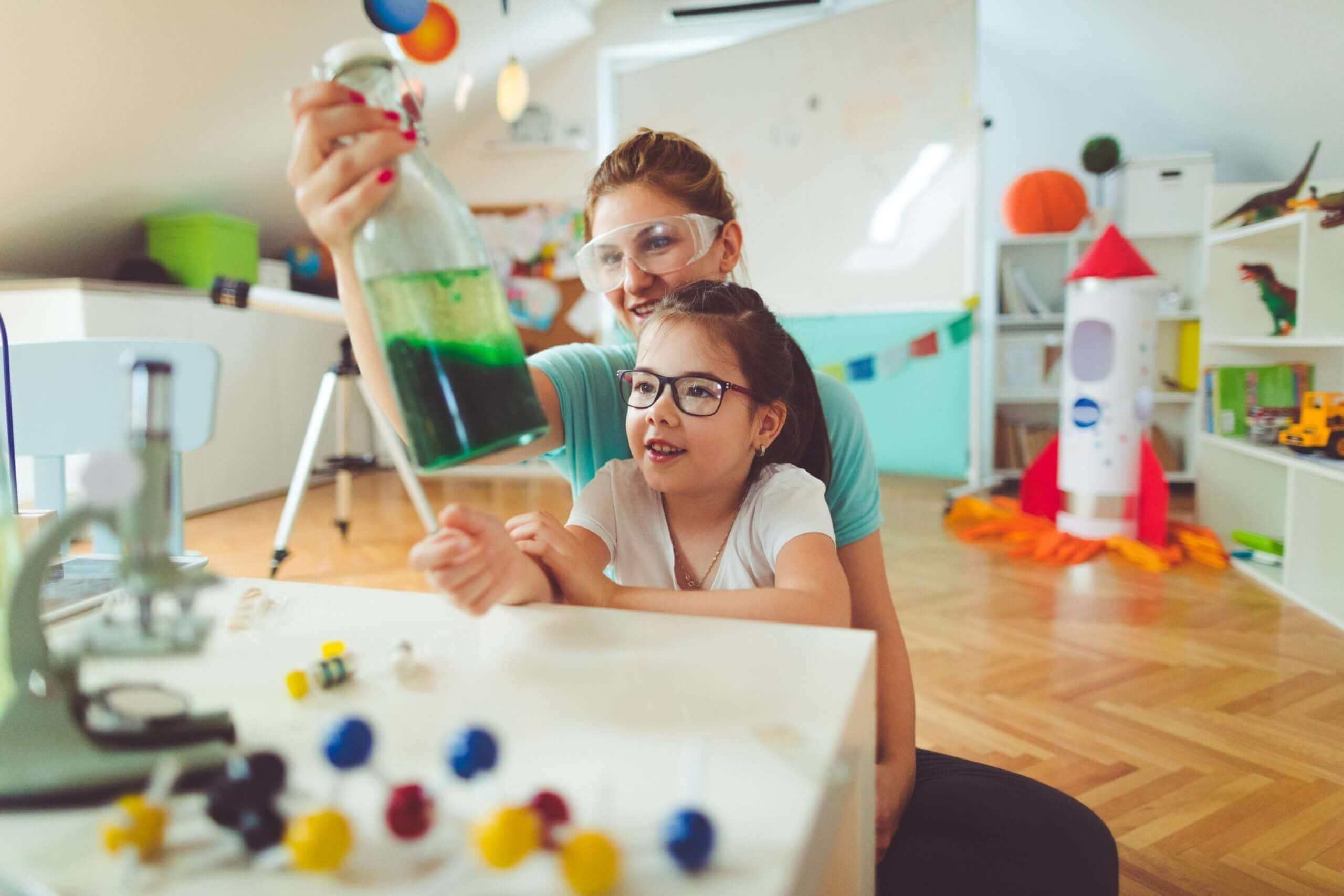 Mãe e filha realizando experimento científico com frascos coloridos em ambiente divertido e educativo.
