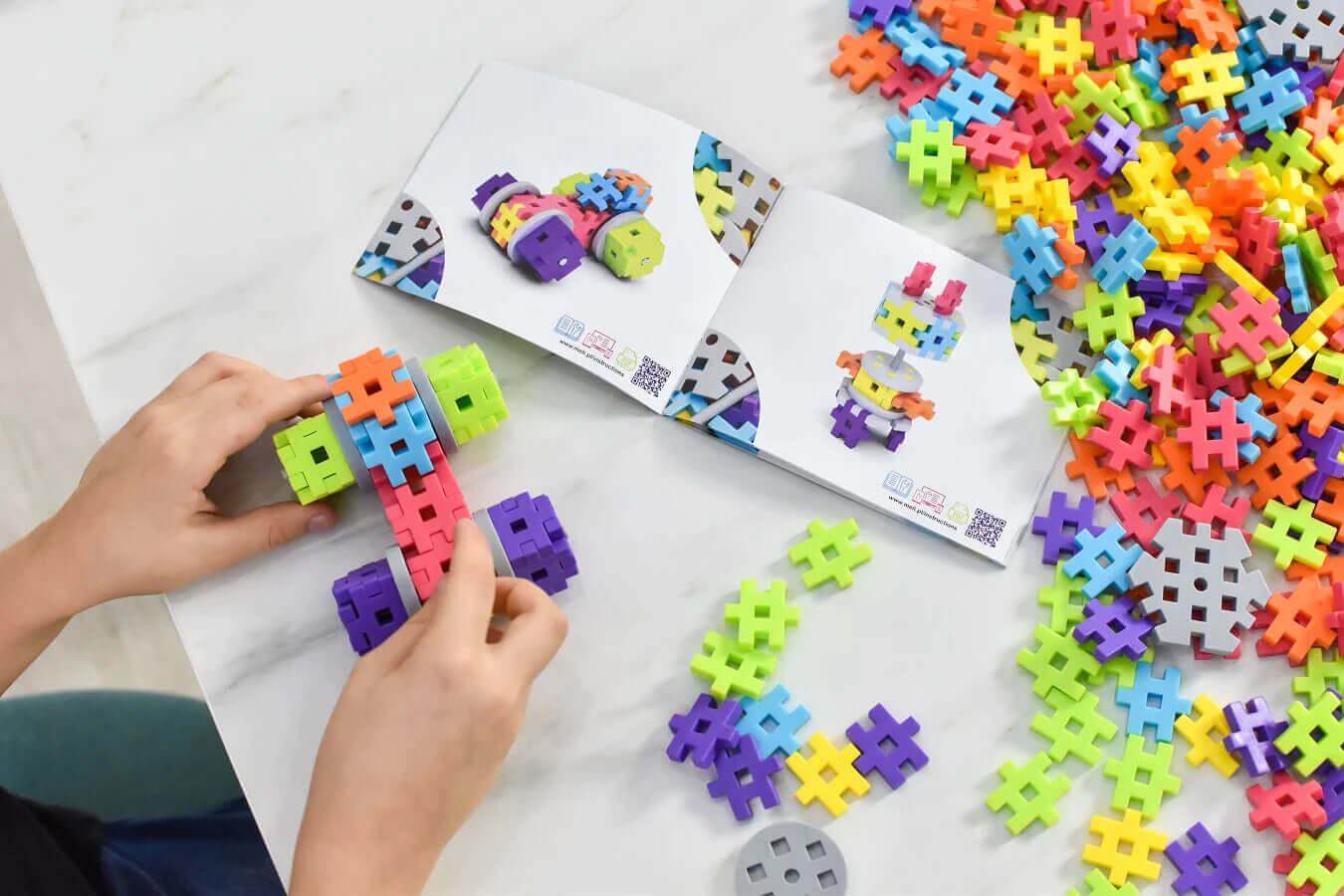 Child building a colorful Meli Blocks creation with a guidebook and scattered blocks on a table.