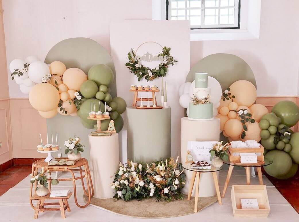 Decoração moderna de baby shower com balões, bolos e mesas elegantes em tons suaves de verde e bege.