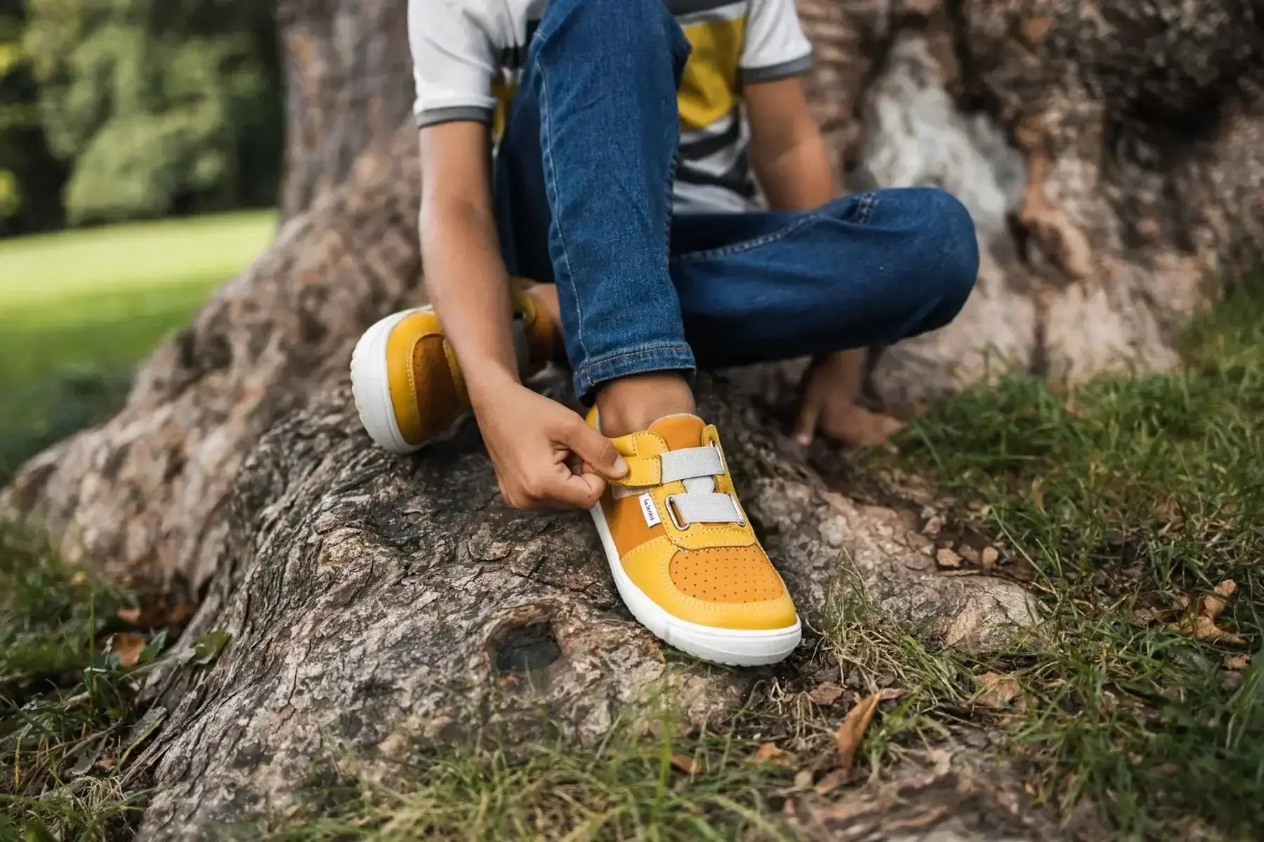 Criança amarrando calçado infantil amarelo em ambiente natural, ideal para conforto e desenvolvimento saudável dos pés.