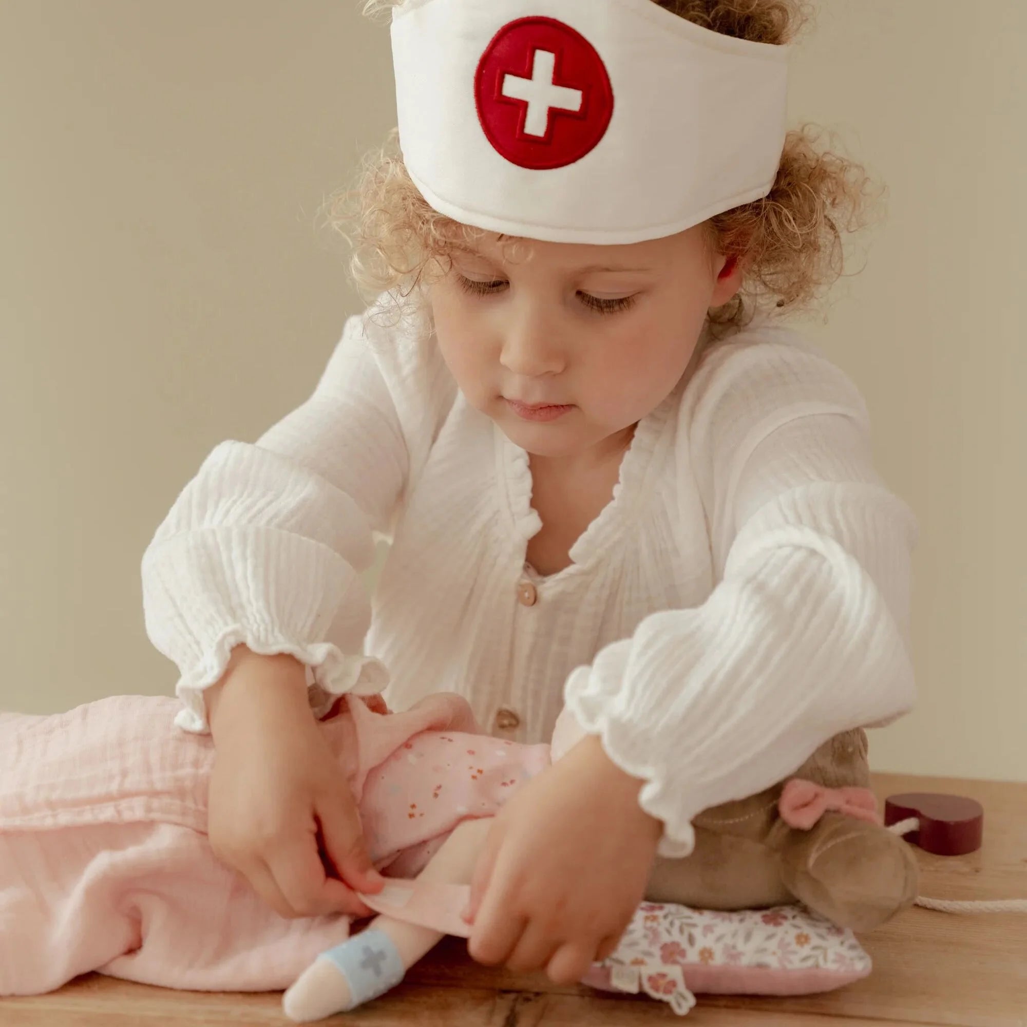 Child playing doctor with nurse hat, tending to a stuffed animal on a table, inspiring imaginative play.