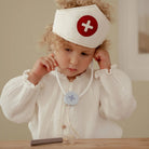 Criança usando um gorro de médico com estetoscópio e acessórios de brinquedo na brincadeira de faz de conta.