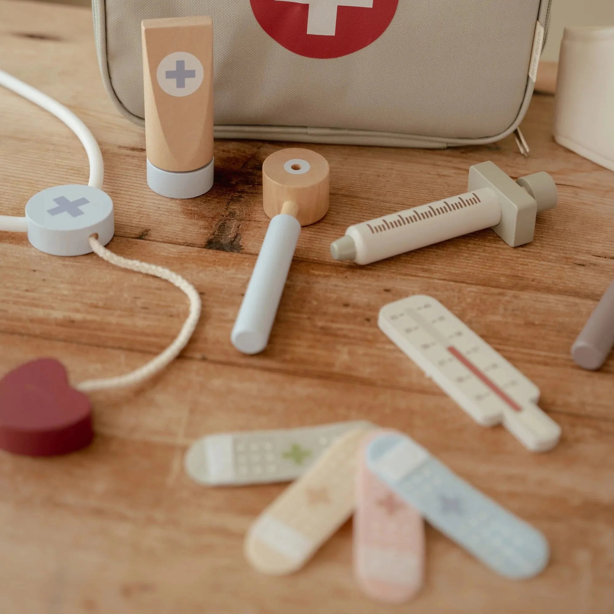 Conjunto de médico em madeira Little Dutch, incluindo estetoscópio, termômetro e band-aids coloridos em uma mesa de madeira.