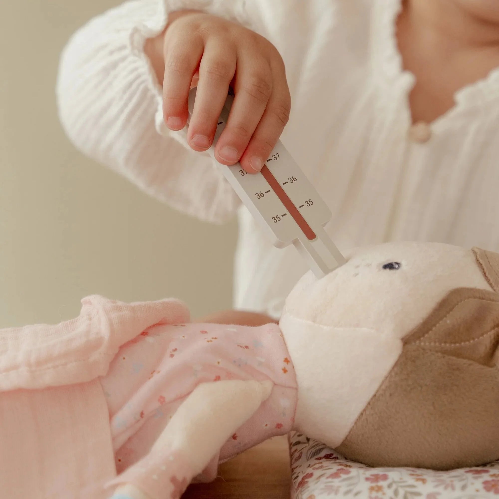 Child using a thermometer on a doll, engaging in imaginative play with the Little Dutch doctor toy set.