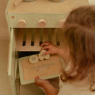 Criança usando o Conjunto de Pasteleiro Little Dutch para brincar na cozinha de madeira.