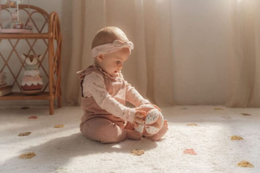 Baby girl sitting on the floor, playing with soft toy balls in a cozy, sunlit room.