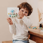 Child holding a colorful craft project featuring soft pom poms, showcasing creativity with Little Dutch art supplies.